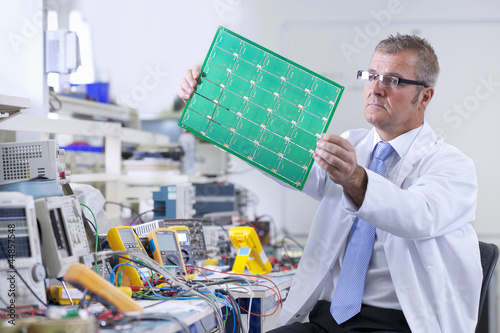 Photo: Engineer examining printed circuit board at electrical test bench Engineer examining printed circuit board at electrical test bench