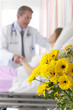 Doctor comforting patient in hospital room, flowers in foreground