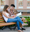 Foto: Young couple sitting on a bench reading a map Young couple sitting on a bench reading a map