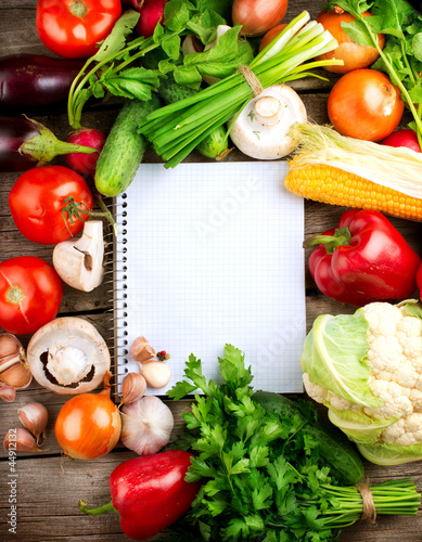 Photo: Open Notebook and Fresh Vegetables Background. Diet Open Notebook and Fresh Vegetables Background. Diet