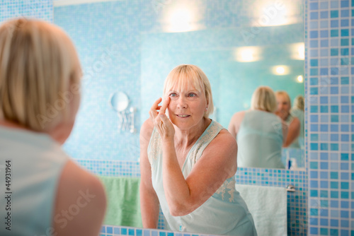 Photo: Female beauty, old woman applying cream on face at home Female beauty, old woman applying cream on face at home