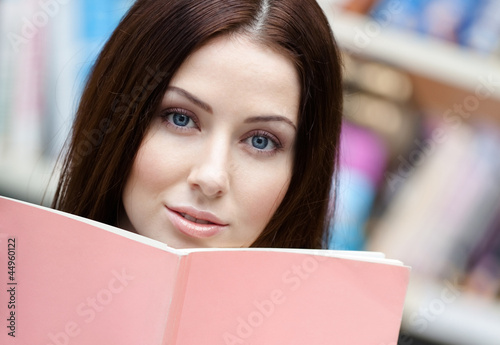 Photo: Female student reads the book at the library. Education Female student reads the book at the library. Education
