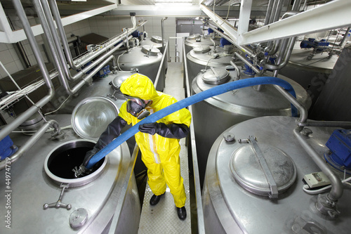 Photo: technician in uniform filling large silver tank in factory technician in uniform filling large silver tank in factory