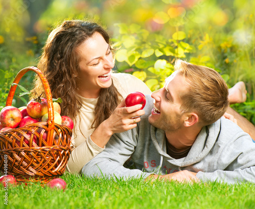Photo: Couple Relaxing on the Grass and Eating Apples in Autumn Garden Couple Relaxing on the Grass and Eating Apples in Autumn Garden