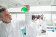 Man viewing liquid while other chemists doing research