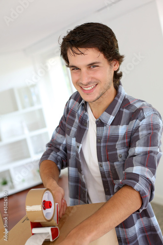 Photo: Young man packing boxes to move in new flat Young man packing boxes to move in new flat