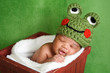 Smiling newborn baby boy wearing a green crocheted frog hat
