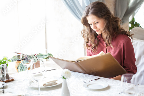 Foto: A woman in a restaurant with the menu in hands A woman in a restaurant with the menu in hands