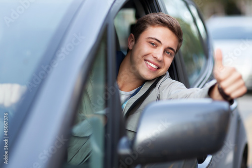 Photo: Young man doing thumps-up in car Young man doing thumps-up in car