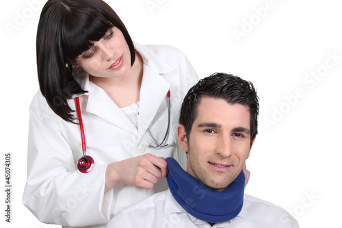Photo: Female doctor applying a neck brace to a male patient Female doctor applying a neck brace to a male patient