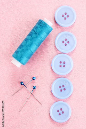 Photo: Colorful sewing buttons with thread on pink fabric Colorful sewing buttons with thread on pink fabric