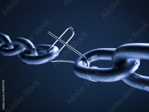 Photo: Chain linked with broken paper clip against blue background Chain linked with broken paper clip against blue background