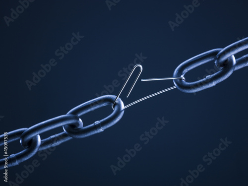 Photo: Chain linked with broken paper clip against blue background Chain linked with broken paper clip against blue background