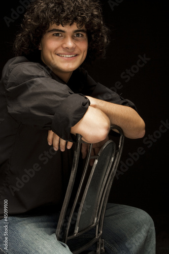 Photo: "Teenage boy (16-17) sitting backwards on chair, portrait" "Teenage boy (16-17) sitting backwards on chair, portrait"