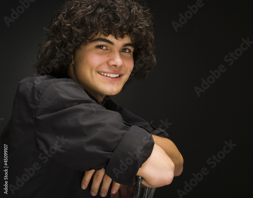 Photo: "Teenage boy (16-17) sitting backwards on chair, portrait" "Teenage boy (16-17) sitting backwards on chair, portrait"