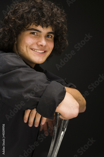 Photo: "Teenage boy (16-17) sitting backwards on chair, portrait" "Teenage boy (16-17) sitting backwards on chair, portrait"