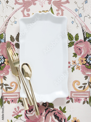 Photo: Empty plate with golden utensils on floral pattern Empty plate with golden utensils on floral pattern