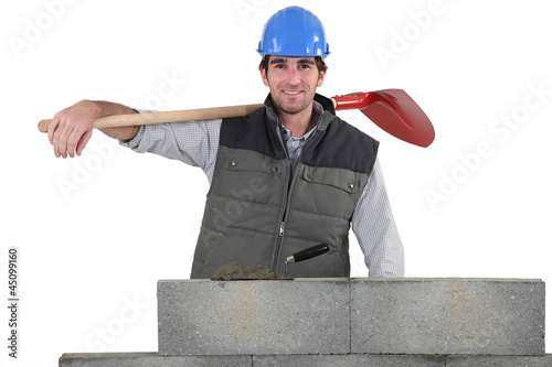 Photo: a handsome bricklayer by brickwall holding shovel a handsome bricklayer by brickwall holding shovel
