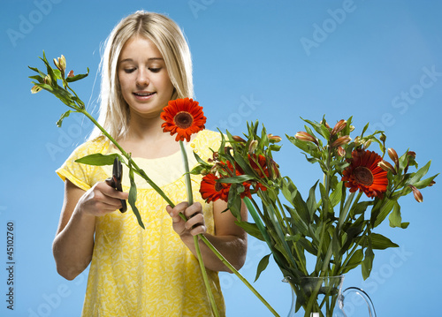 Photo: "Young woman pruning flowers, studio shot" "Young woman pruning flowers, studio shot"