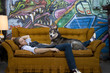 Photo: USA, Utah, Salt Lake City, Young man sleeping on sofa with dog, graffiti in background USA, Utah, Salt Lake City, Young man sleeping on sofa with dog, graffiti in background