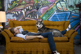 Photo: USA, Utah, Salt Lake City, Young man sleeping on sofa with dog, graffiti in background USA, Utah, Salt Lake City, Young man sleeping on sofa with dog, graffiti in background