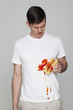 Young man wearing stained t-shirt holding hot-dog