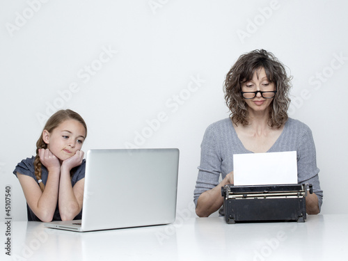 Photo: Studio shot of mother using typewriter and daughter (10-11) looking at laptop Studio shot of mother using typewriter and daughter (10-11) looking at laptop