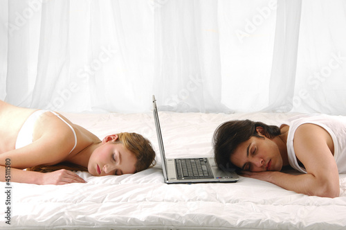 Photo: Couple lying in bed sleeping with laptop Couple lying in bed sleeping with laptop