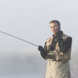man fishing in a river on his cell phone