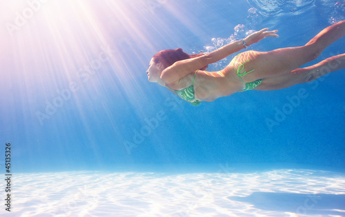 Photo: Woman swimming underwater in a blue pool. Woman swimming underwater in a blue pool.