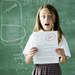 girl in a classroom standing in front of a chalkboard with an a plus paper