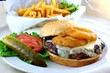 Cheeseburger topped with onion rings with fries.