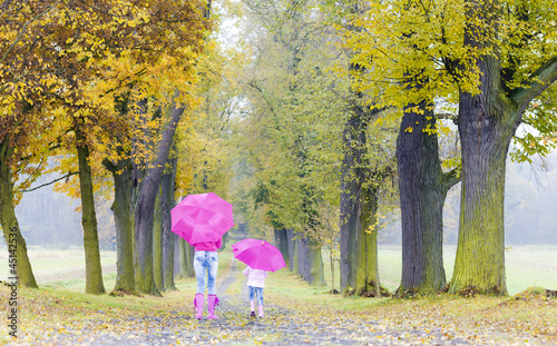 Photo: mother and her daughter with umbrellas in autumnal alley mother and her daughter with umbrellas in autumnal alley