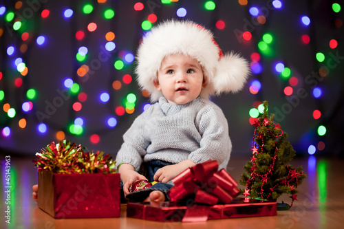 Photo: funny baby in Santa Claus hat on bright festive background funny baby in Santa Claus hat on bright festive background