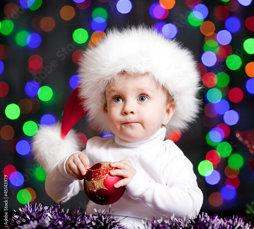 Photo: funny baby in Santa Claus hat on bright festive background funny baby in Santa Claus hat on bright festive background