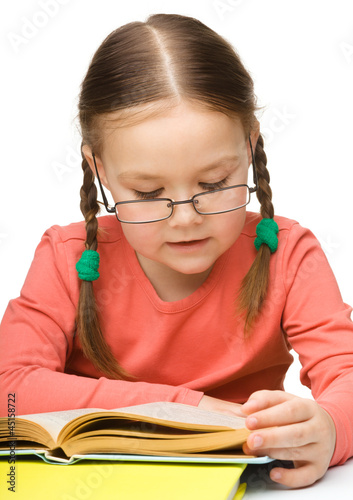 Photo: Cute little girl reading book wearing glasses Cute little girl reading book wearing glasses