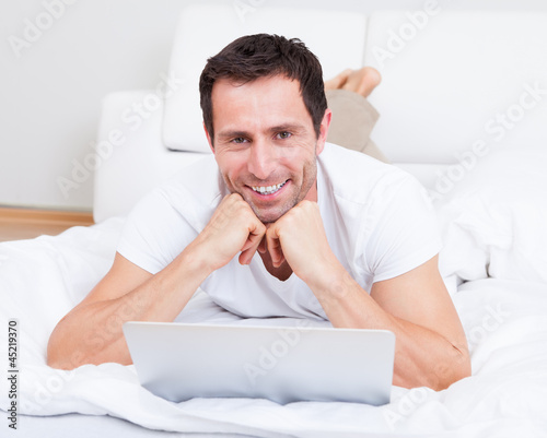 Photo: Portrait Of Young Man Lying On Bed Using Laptop Portrait Of Young Man Lying On Bed Using Laptop