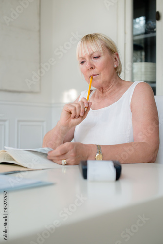 Photo: Mature woman checking bills and doing budget at home Mature woman checking bills and doing budget at home