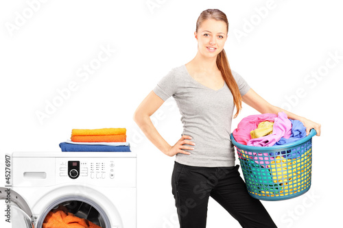 Photo: Woman holding a laundry basket next to a washing machine Woman holding a laundry basket next to a washing machine