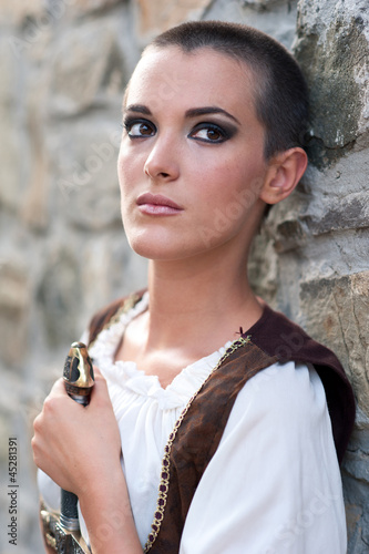 Photo: Beautiful girl wearing a medieval dress. Stone wall background. Beautiful girl wearing a medieval dress. Stone wall background.