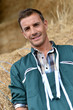 Portrait of smiling farmer standing by haystacks