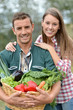 Portrait of couple of farmers holding basket of vegetables