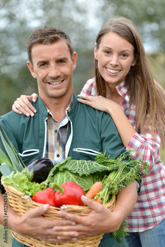 Photo: Portrait of couple of farmers holding basket of vegetables Portrait of couple of farmers holding basket of vegetables