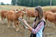 Woman farmer in front of cattle using tablet
