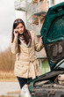 Woman looking under car hood on phone
