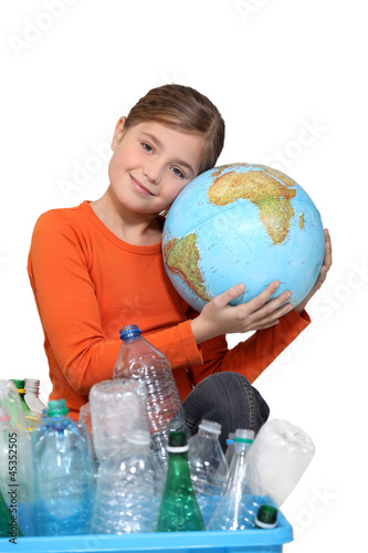 Photo: Young girl hugging a globe behind a box of plastic recycling Young girl hugging a globe behind a box of plastic recycling