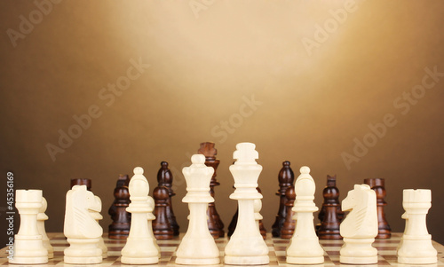 Photo: Chess board with chess pieces on brown background Chess board with chess pieces on brown background