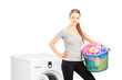 Smiling woman with laundry basket posing next to a washing machi