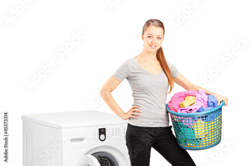 Photo: Smiling woman with laundry basket posing next to a washing machi Smiling woman with laundry basket posing next to a washing machi