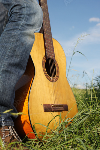 Photo: Wooden guitar resting on a mans foot in long green Wooden guitar resting on a mans foot in long green